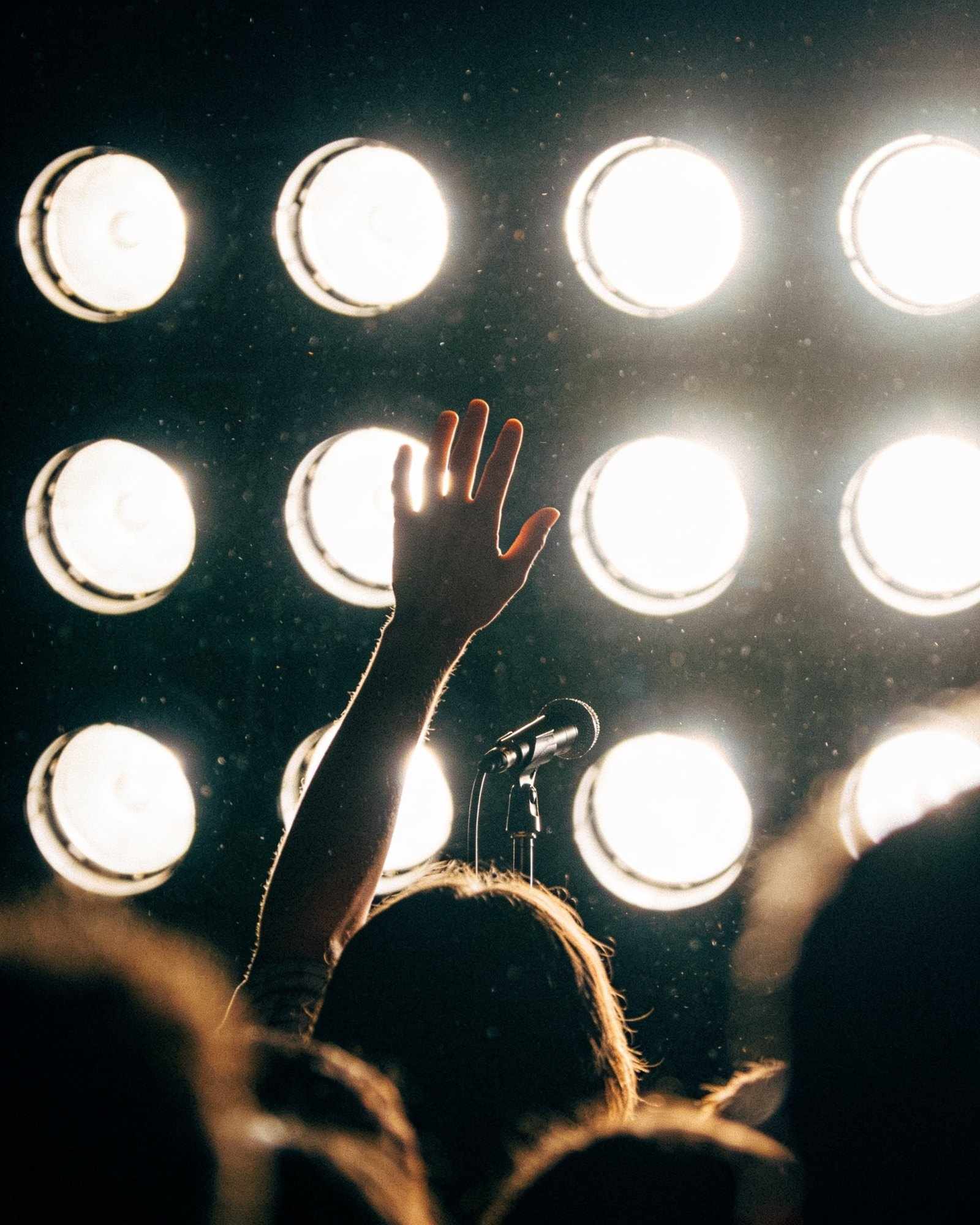 A raised hand and a microphone in front of a wall of bright round stage lights
