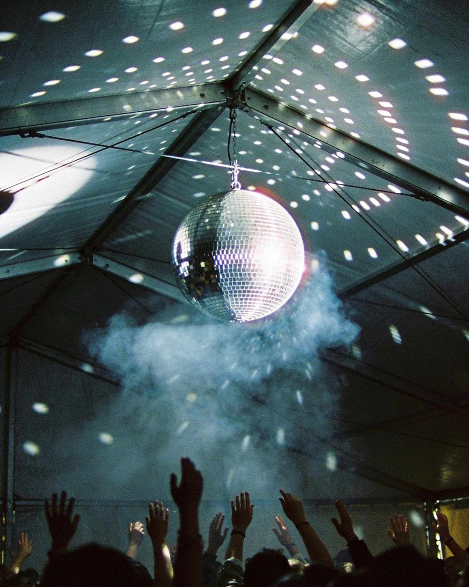 A disco ball scattering spots of light over a dark tent roof and a haze of dry ice